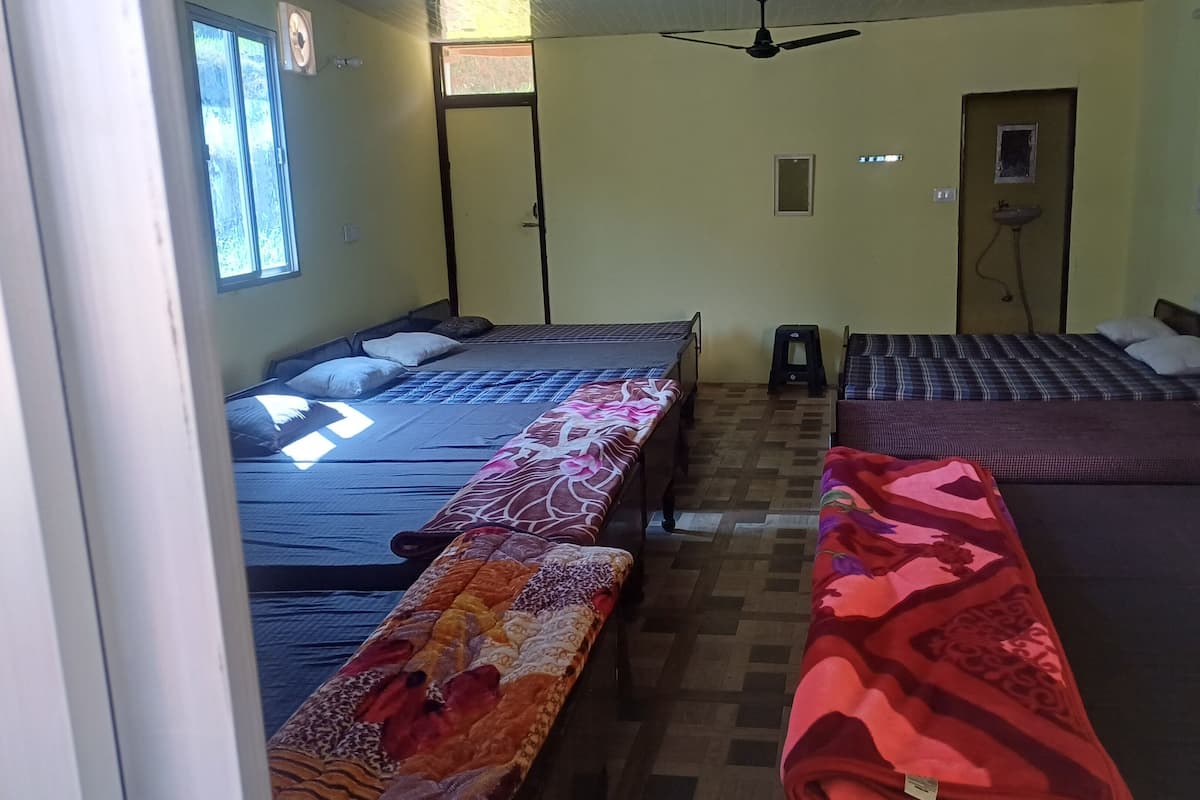 A room with three beds, a ceiling fan, a window, and a door.