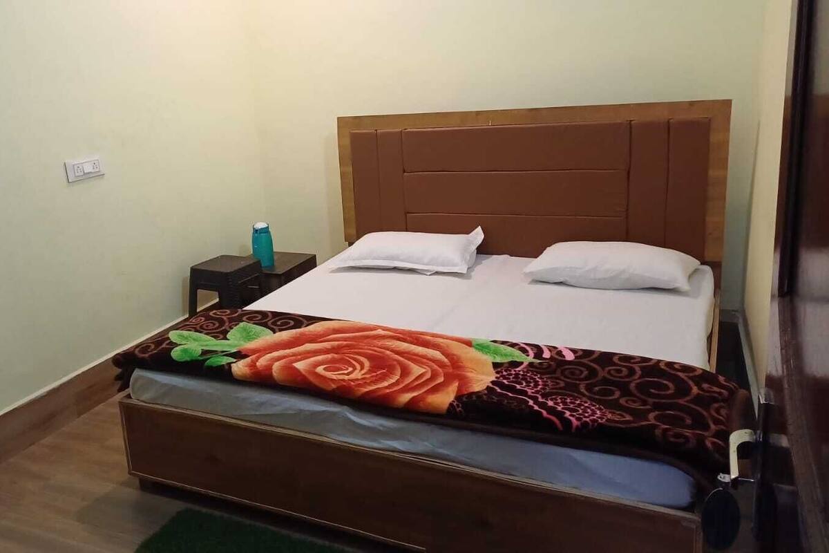 A bed with a floral bedspread, a nightstand with a bottle, and a wall-mounted light switch.