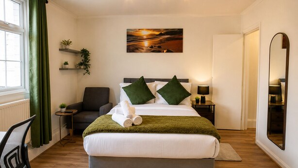 Una habitación de hotel con una cama, una silla, un escritorio, un espejo y un cuadro en la pared.