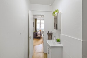 Ein schmaler Gang führt zu einem Raum mit Schreibtisch, Stuhl und Fenster.