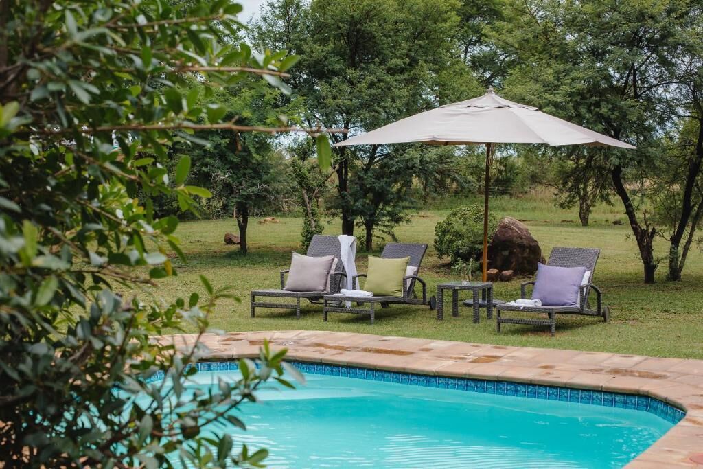 A swimming pool with lounge chairs and a table, surrounded by greenery.