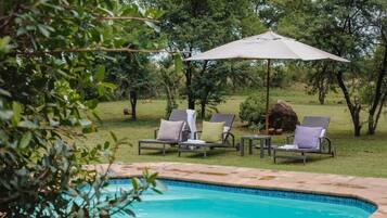 A swimming pool with lounge chairs and a table, surrounded by greenery.