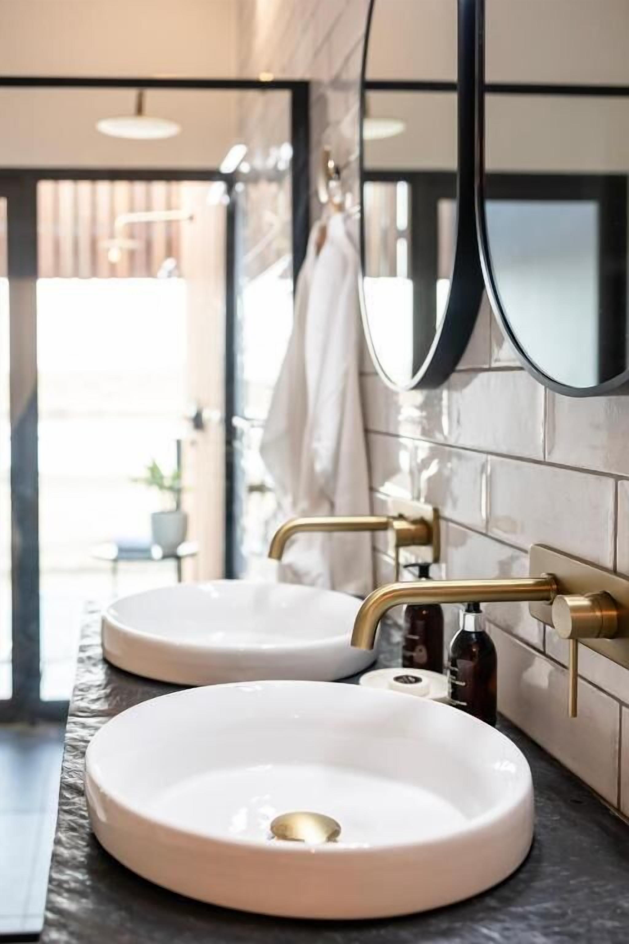 A bathroom with two round white sinks, a large mirror, and a gold faucet.