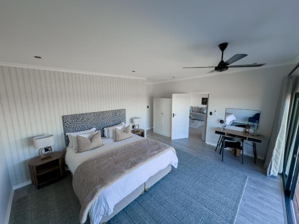 Ein modernes Hotelzimmer mit einem großen Bett, einem Schreibtisch, einem Deckenventilator und Blick ins angrenzende Badezimmer.