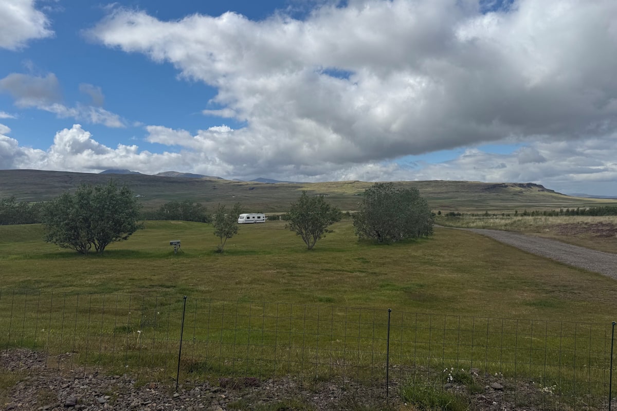 A rural landscape with rolling hills, a fenced field, and a white caravan.