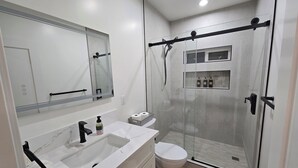 A modern bathroom with a shower enclosure, a toilet, a sink with a mirror, and a towel rack. - Cozy Guesthouse Near Disneyland in Walking Distance (Garden Grove)