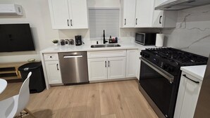 A modern kitchen with white cabinets, stainless steel appliances, a black stove, and a microwave. - Cozy Guesthouse Near Disneyland in Walking Distance (Garden Grove)