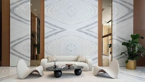 A modern living room with a marble-patterned wall, a sofa, two chairs, and a coffee table. - Bloomfields Studio - Binghatti Azure JVC (Dubai)