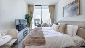 A modern hotel room with a large bed, a television, a dining table, and a city view. - Bloomfields Studio - Binghatti Azure JVC (Dubai)