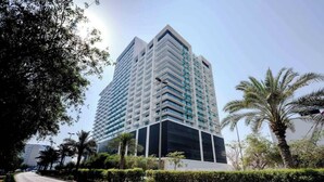 A high-rise building with a modern architectural design, surrounded by greenery and a clear sky. - Bloomfields Studio - Binghatti Azure JVC (Dubai)