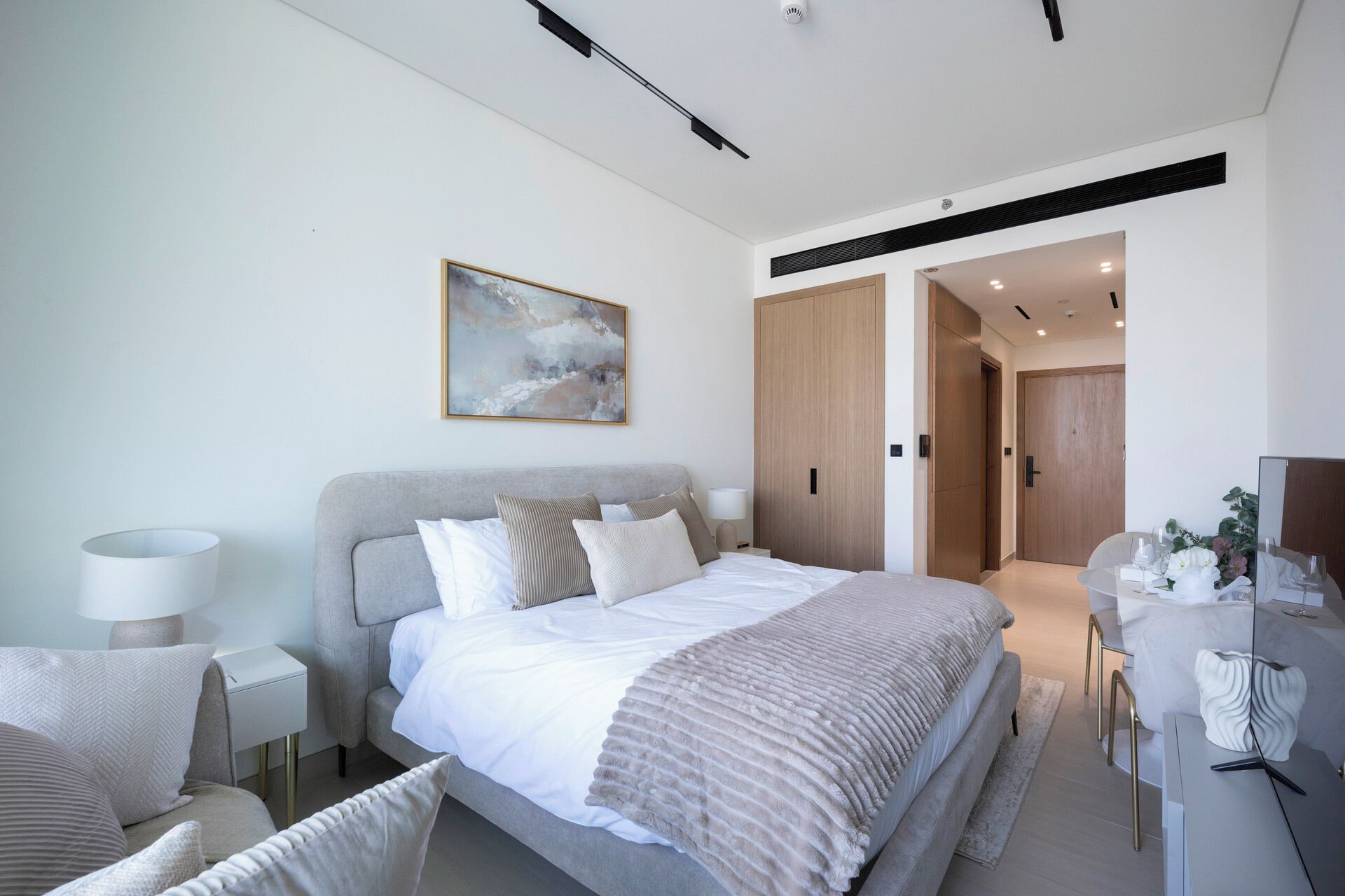 Quarto moderno com cama, mesas de cabeceira, poltrona, escrivaninha e um quadro na parede.