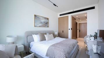 Quarto moderno com cama, mesas de cabeceira, poltrona, escrivaninha e um quadro na parede.