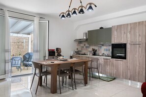 Una cuina moderna amb armaris de fusta, zona de menjador amb taula i cadires, i una porta corredissa de vidre que dona a un patio exterior.