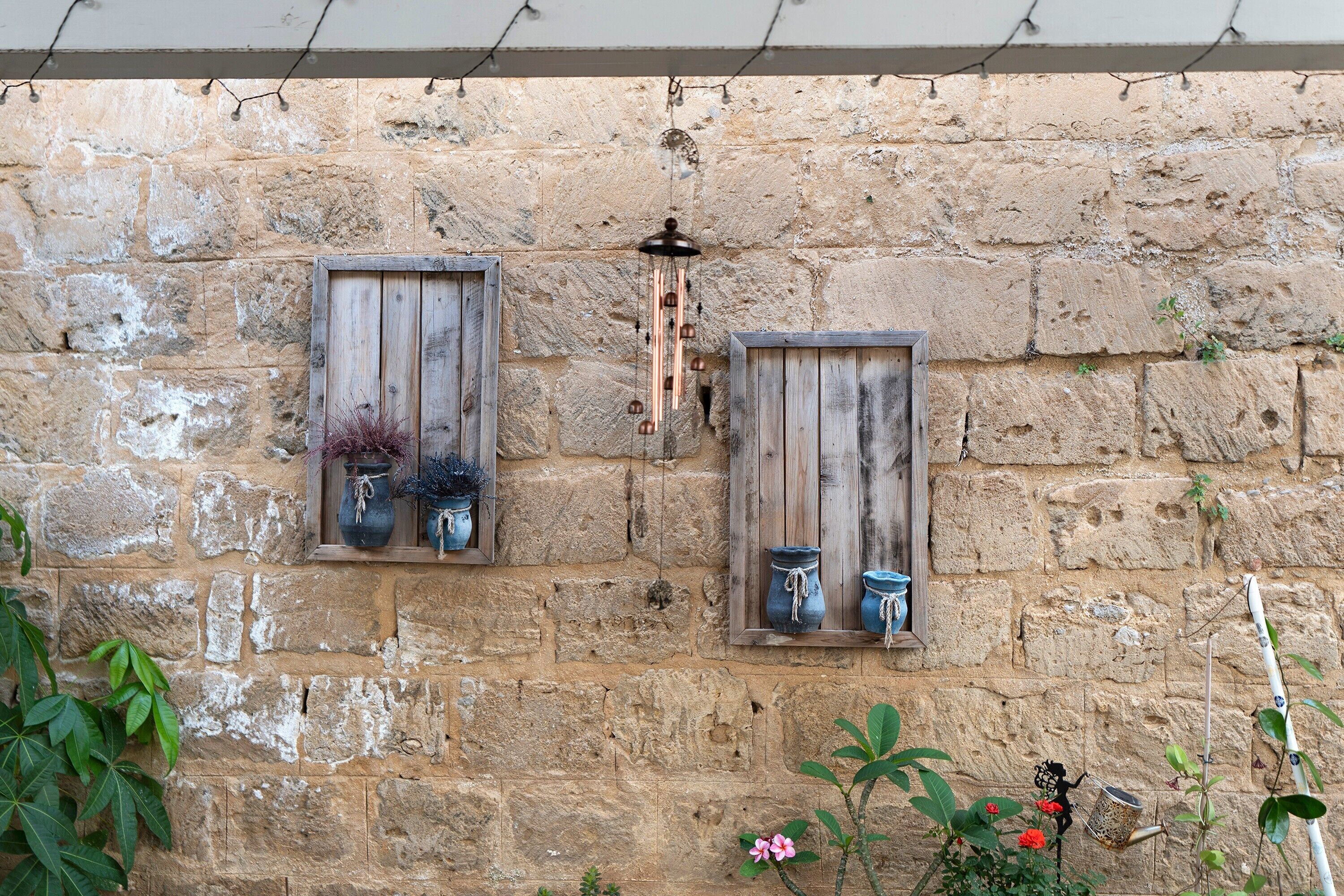 Una pared de piedra rústica con dos marcos de madera para ventanas, cada uno con una maceta.
