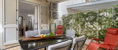 An outdoor patio with a glass-top table, grey and red chairs, and a white ceiling.