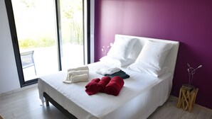 A neatly made bed with white and red towels, a bedside table with a lamp, and a view through a large window. - Between Sea and Pine Forest (Pool, Spa Jacuzzi, Sauna) – Aubergine Room (Bandol)