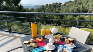 A breakfast table with a variety of food and drinks, a teapot, and a glass of orange juice on a balcony overlooking a forested area. - Between Sea and Pine Forest (Pool, Spa Jacuzzi, Sauna) – Aubergine Room (Bandol)