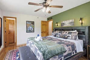 A bedroom with a bed, a ceiling fan, a green wall, and a wooden door. - Webster Lodge at Covemont | Smoky Mountain Getaway (Sevierville)
