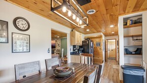 A wooden dining table with chairs, a clock, and framed pictures on the wall. - Webster Lodge at Covemont | Smoky Mountain Getaway (Sevierville)
