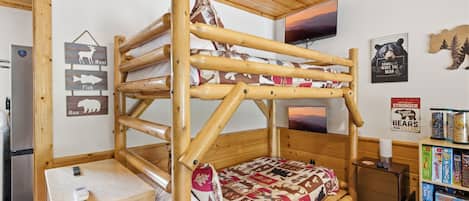 A bunk bed with a quilt, a small wooden cabinet, a television, and a bookshelf with books.