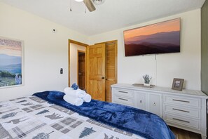 A bedroom with a bed, a TV, a wooden door, and a white dresser. - Webster Lodge at Covemont | Smoky Mountain Getaway (Sevierville)