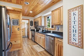 A modern kitchen with wooden cabinets, stainless steel appliances, and a chalkboard menu. - Webster Lodge at Covemont | Smoky Mountain Getaway (Sevierville)