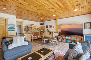 A cozy cabin interior with a bunk bed, a television, and a large window with a sunset view. - Webster Lodge at Covemont | Smoky Mountain Getaway (Sevierville)