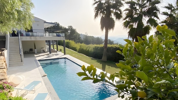 Una piscina rectangular con sillas de descanso, un área de estar techada y vistas del paisaje circundante.