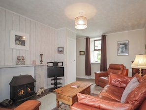 A living room with a fireplace, leather sofa, wooden coffee table, and a television. - Keepers Cottage (Peterhead)