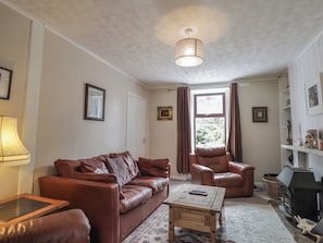 A living room with a brown leather sofa, a wooden coffee table, a fireplace, and a patterned rug. - Keepers Cottage (Peterhead)