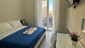 Ein Hotelzimmer mit Bett, Schreibtisch, Stuhl, Zimmerpflanze und Blick ins Freie.
