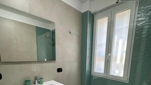 Ein modernes Badezimmer mit einem großen Spiegel, einem Waschbecken, einer Holz-Waschkommode, einer Dusche mit Glastür und einer Toilette.
