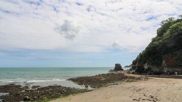 Una playa con costas rocosas, cielo despejado y una formación rocosa distante.