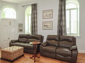 A living room with two leather sofas, a floral ottoman, a wooden coffee table, and framed pictures on the walls. - Farthings, The Old Chapel (St Austell)