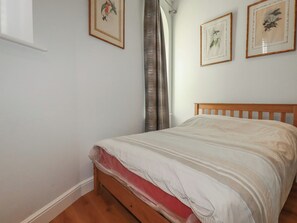 Un dormitorio con cama de madera, paredes blancas y tres láminas enmarcadas con motivos botánicos.