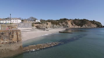 Un paysage côtier avec une plage de sable, un mur de pierre et un bâtiment avec des marches descendant vers l’eau.