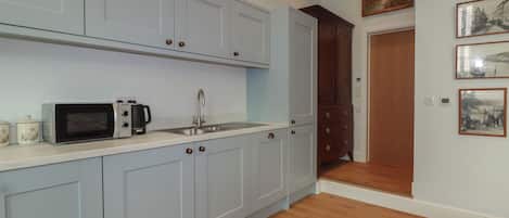 A kitchen with light blue cabinets, a microwave, a sink, and wooden flooring.