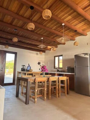 A kitchen with wooden beams, a dining table with chairs, a refrigerator, and hanging wicker light fixtures. - Beachfront House with Private Pool, near Troncones (Gro.)
