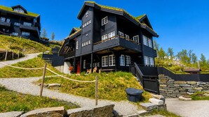 Un bâtiment en bois à plusieurs étages, doté d’un toit à forte pente, de murs en pierre et d’un chemin de gravier menant à l’entrée.