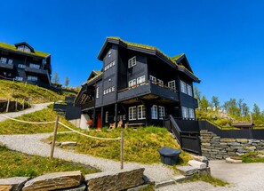 A multi-story wooden building with a steeply pitched roof, stone walls, and a gravel pathway leading to the entrance. - Kikut Apartment - close to ski slopes (Hol)