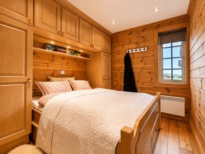 Un dormitorio con paneles de madera, una cama, estanterías empotradas, un radiador y una ventana.