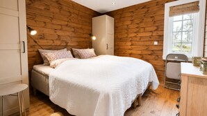 Une chambre avec un mur en bois, un lit avec une literie blanche, une petite table et une fenêtre donnant sur un paysage agréable.