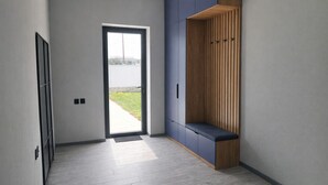 Un pasillo con una puerta que da al exterior, un banco con ganchos y un mueble de pared con armarios.