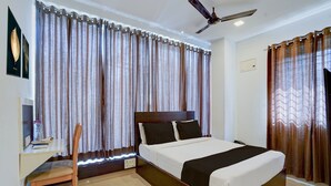 A hotel room with a bed, a desk with a chair, a ceiling fan, and curtains. - Townhouse Bannerghatta Hospital Road (Bengaluru)