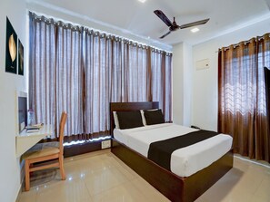 Ein Hotelzimmer mit Bett, Schreibtisch mit Stuhl, Deckenventilator und Vorhängen.