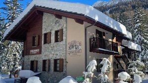 A stone building with a wooden facade, labeled "Wild Wolf Lodge," surrounded by snow-covered trees and mountains. - Wildhomes Wild Wolf Lodge: Nestled in the Peuterey Forest—Up to 6 Guests (Courmayeur)