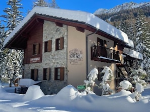 Ein Steinhaus mit Holzfassade, mit der Aufschrift "Wild Wolf Lodge“, umgeben von schneebedeckten Bäumen und Bergen.