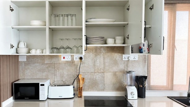 A modern kitchen with white cabinets, a microwave, toaster, and a blender on the counter.