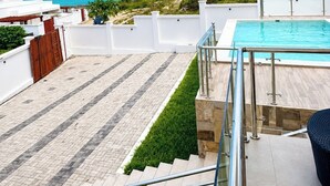A rooftop pool with a clear view of the ocean, a tiled patio, and a staircase leading to the pool area.