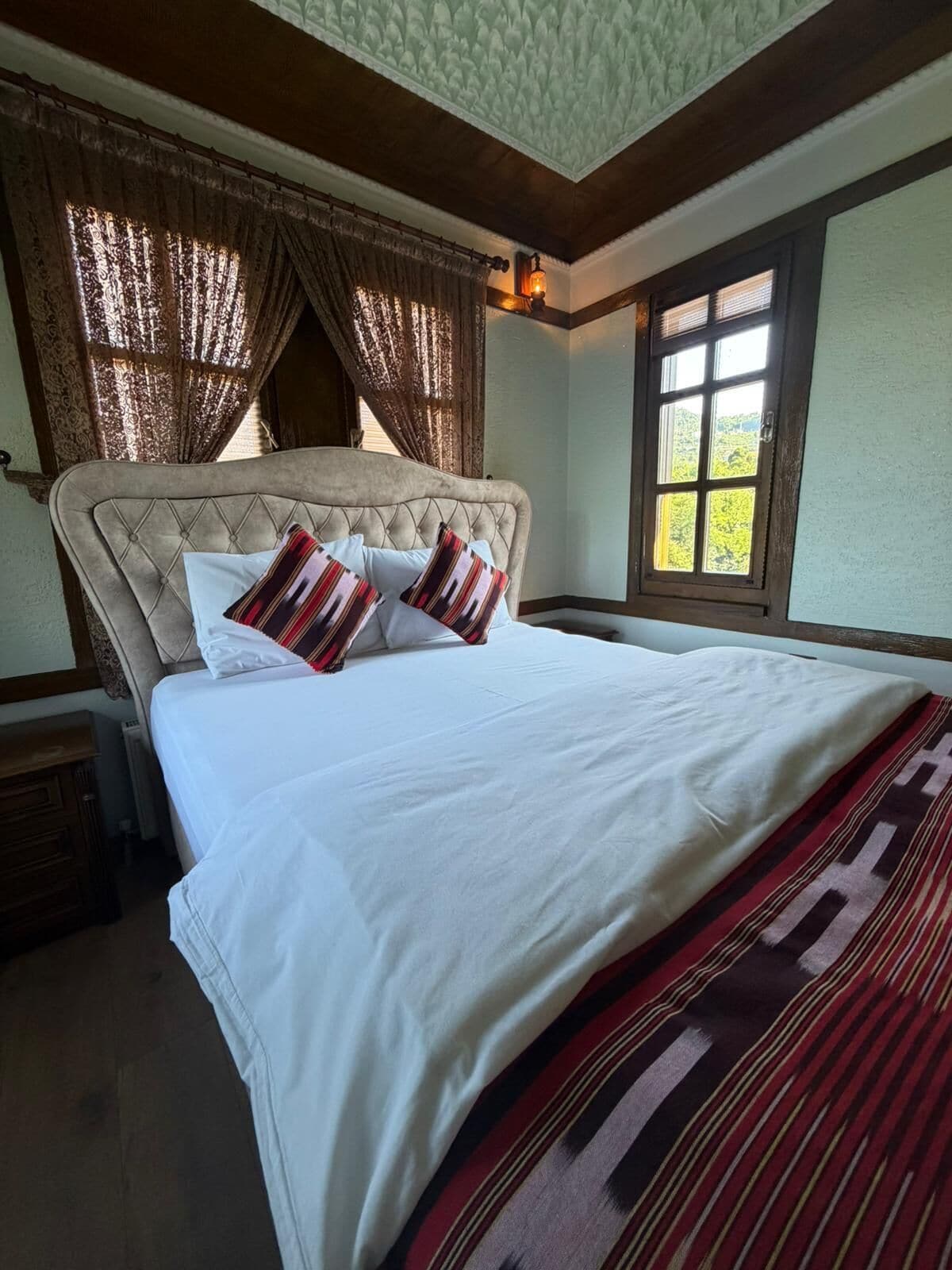 A bedroom with a large bed, a window with a view, and a wooden ceiling.